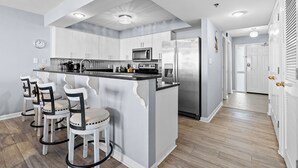Una cocina moderna con armarios blancos, una isla central con taburetes de bar, electrodomésticos de acero inoxidable y suelo de madera.