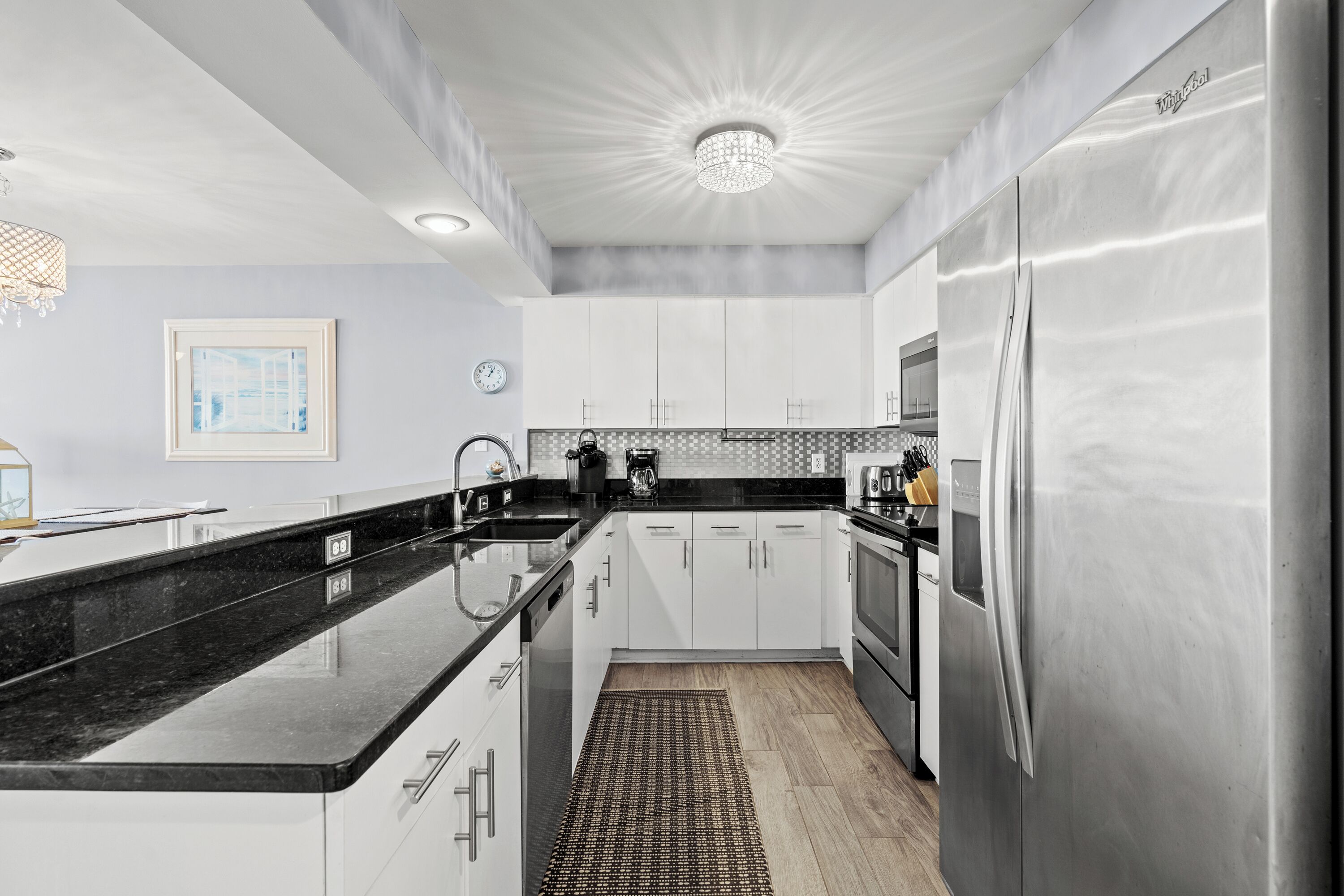 A modern kitchen with white cabinets, a stainless steel refrigerator, and a black granite countertop.