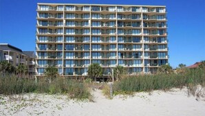 Un hotel de varios pisos con fachada uniforme, balcones y ubicación frente a la playa.