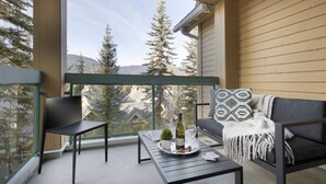 Een balkon met een bank, een stoel en een tafel met een fles en glazen.