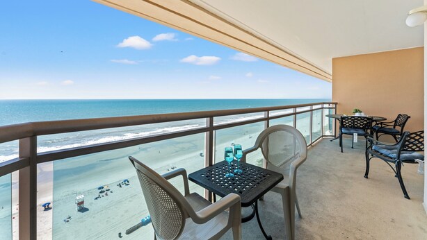 A balcony with a view of the beach, two chairs, a table, and a pair of glasses. - Bahama Sands Luxury Villas PH6-3BR/3BA Oceanfront condo in Crescent Beach (North Myrtle Beach)