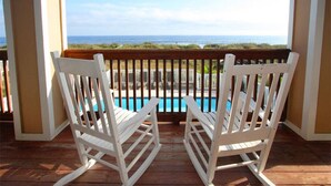 Twee schommelstoelen op een houten terras met uitzicht op een zwembad en de oceaan.