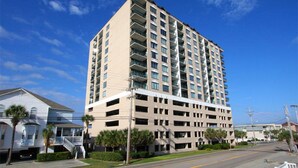 A high-rise building with multiple floors, balconies, and a parking garage. - Beachwalk Villas 808-2BR/2BA Condo in Cherry Grove (North Myrtle Beach)