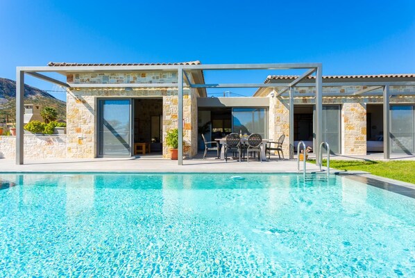 A modern poolside area with a clear pool, stone walls, and a covered seating area.
