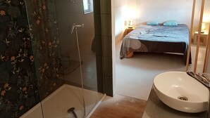 Une salle de bain avec une douche, un lavabo et un lit recouvert d’une couverture bleue.