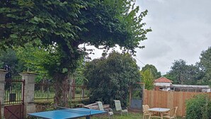 Un jardin avec une table de ping-pong, des chaises, une table en bois et une clôture.