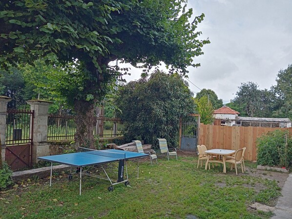A backyard with a ping pong table, chairs, a wooden table, and a fence.