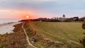 A coastal landscape with a grassy field, a path, and a building with a tower. - The Hideout (Chichester)