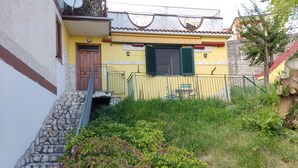 Une maison à deux étages avec un escalier en pierre, une façade jaune et une porte verte.