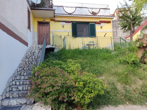 A two-story house with a stone staircase, a yellow facade, and a green door.