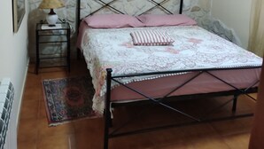 Une chambre avec un mur en pierre, un lit avec un cadre en métal, une table de chevet avec une lampe et un miroir au-dessus du lit.