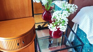 Une pièce de taille modeste, avec un banc en bois, une table à plateau de verre surmontée de deux vases rouges et un lit à motifs bleus.