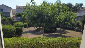 A view from a balcony overlooking a garden with a hedge, a tree, and a building in the background. - House 6 pers. direct beach access(100 meters walk) (Borgo)