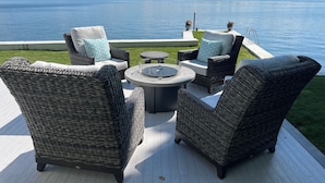 Een terras met rieten meubilair en een vuurkuil, met uitzicht op een meer.