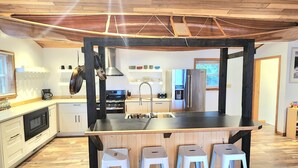 A modern kitchen with a central island, wooden ceiling, and bar stools.
