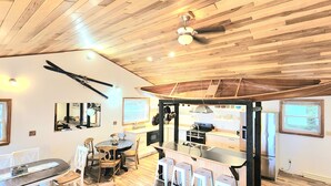 A modern kitchen with wooden ceiling, a dining area with a round table and chairs, and a large window.