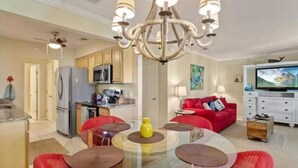 A modern living room with a glass dining table, red chairs, a chandelier, and a red sofa.