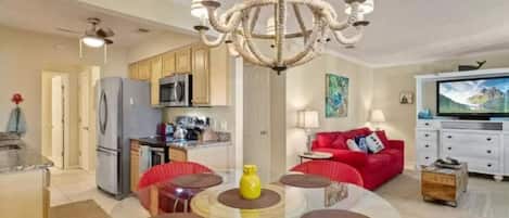 A modern living room with a glass dining table, red chairs, a chandelier, and a red sofa.