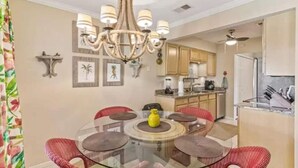 A dining area with a glass table surrounded by red chairs, a chandelier, and framed pictures on the wall.