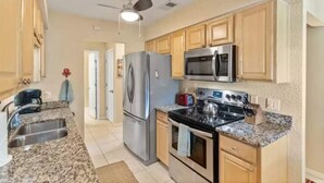 A kitchen with granite countertops, stainless steel appliances, wooden cabinets, and a ceiling fan.
