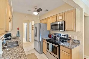 Compact kitchen with a gas stove, microwave, and refrigerator, featuring a sink and granite countertops.