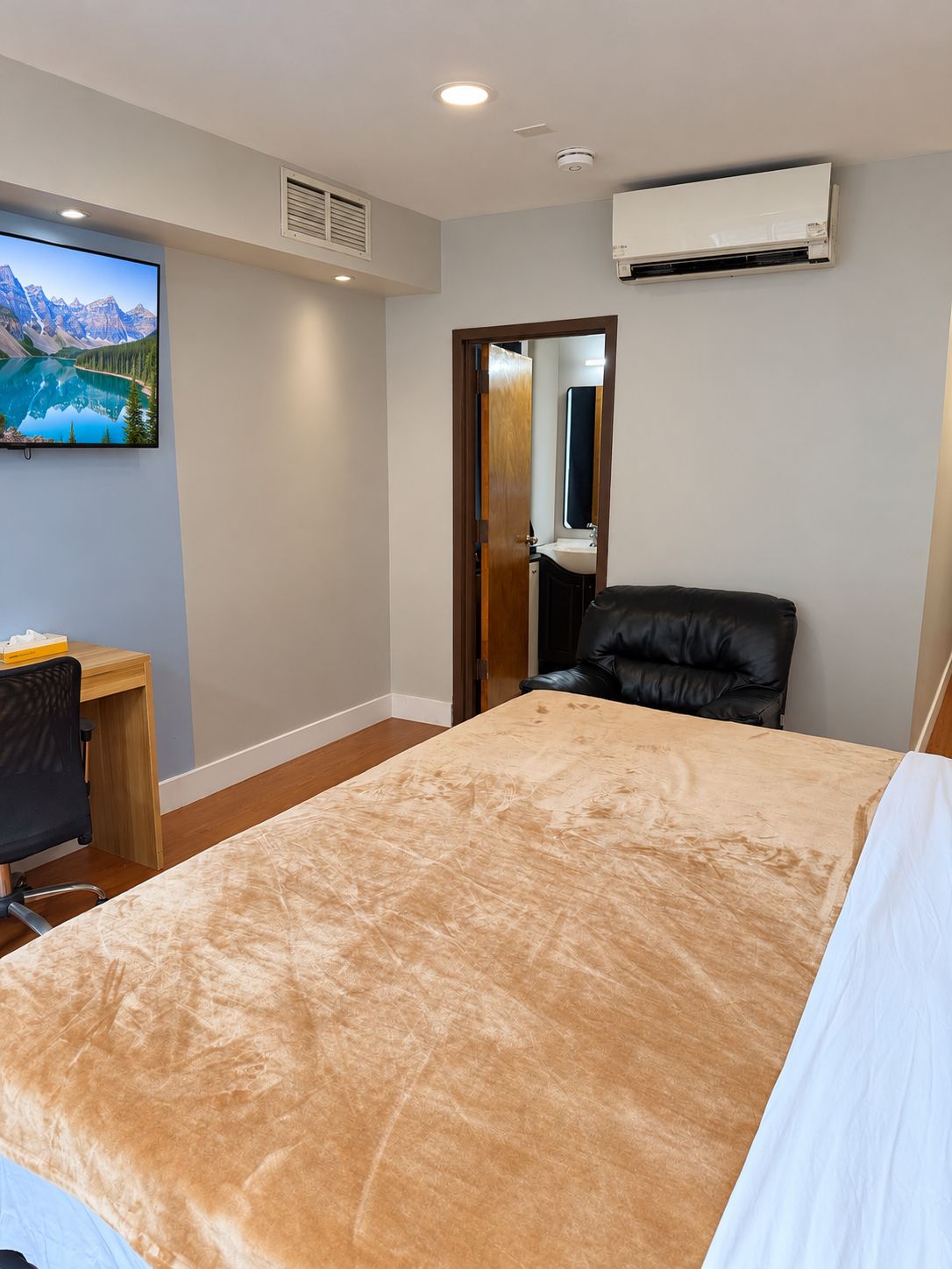Una habitación de hotel con cama, escritorio, silla, televisor y aire acondicionado.