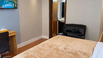 Una habitación de hotel con cama, escritorio, silla, televisor y aire acondicionado.