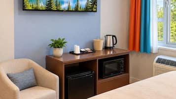 Habitación de hotel con cama, escritorio con computadora, una silla, televisor montado en la pared y ventana con cortinas.