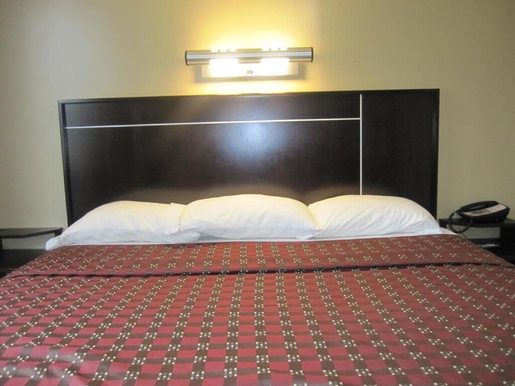 Ein Hotelzimmer mit einem großen Bett, einem Kopfteil mit einer Leuchte und einem Telefon auf einem Nachttisch.