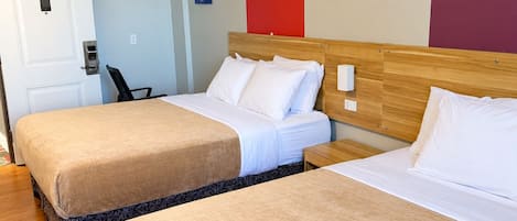 Habitación de hotel con dos camas, cabecera de madera, puerta blanca y una obra de arte en la pared.