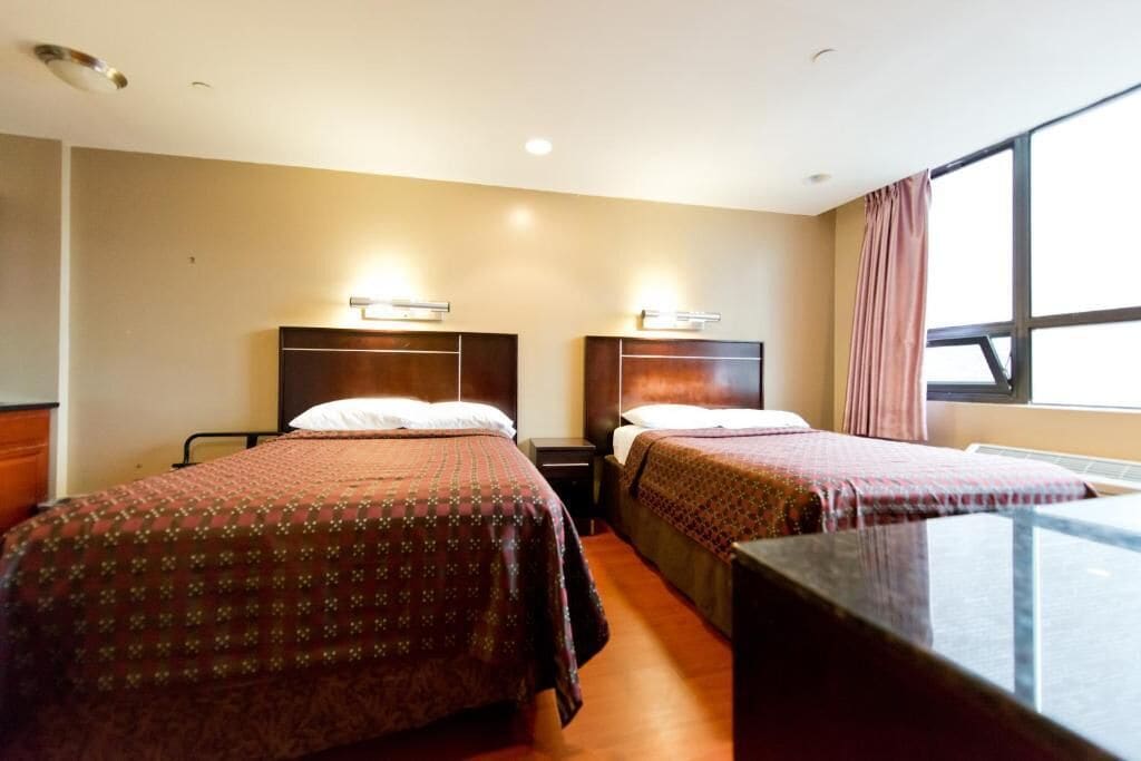 A hotel room with two beds, a desk, and a window with curtains.