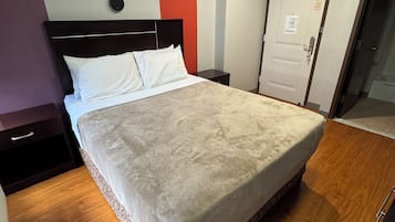 Una habitación de hotel con una cama grande, una mesita de noche, una puerta y un aplique de pared.