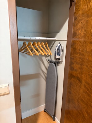 Ein Schrank mit Holz-Kleiderbügeln, ein graues Bügelbrett und ein an der Wand befestigtes Bügeleisen.