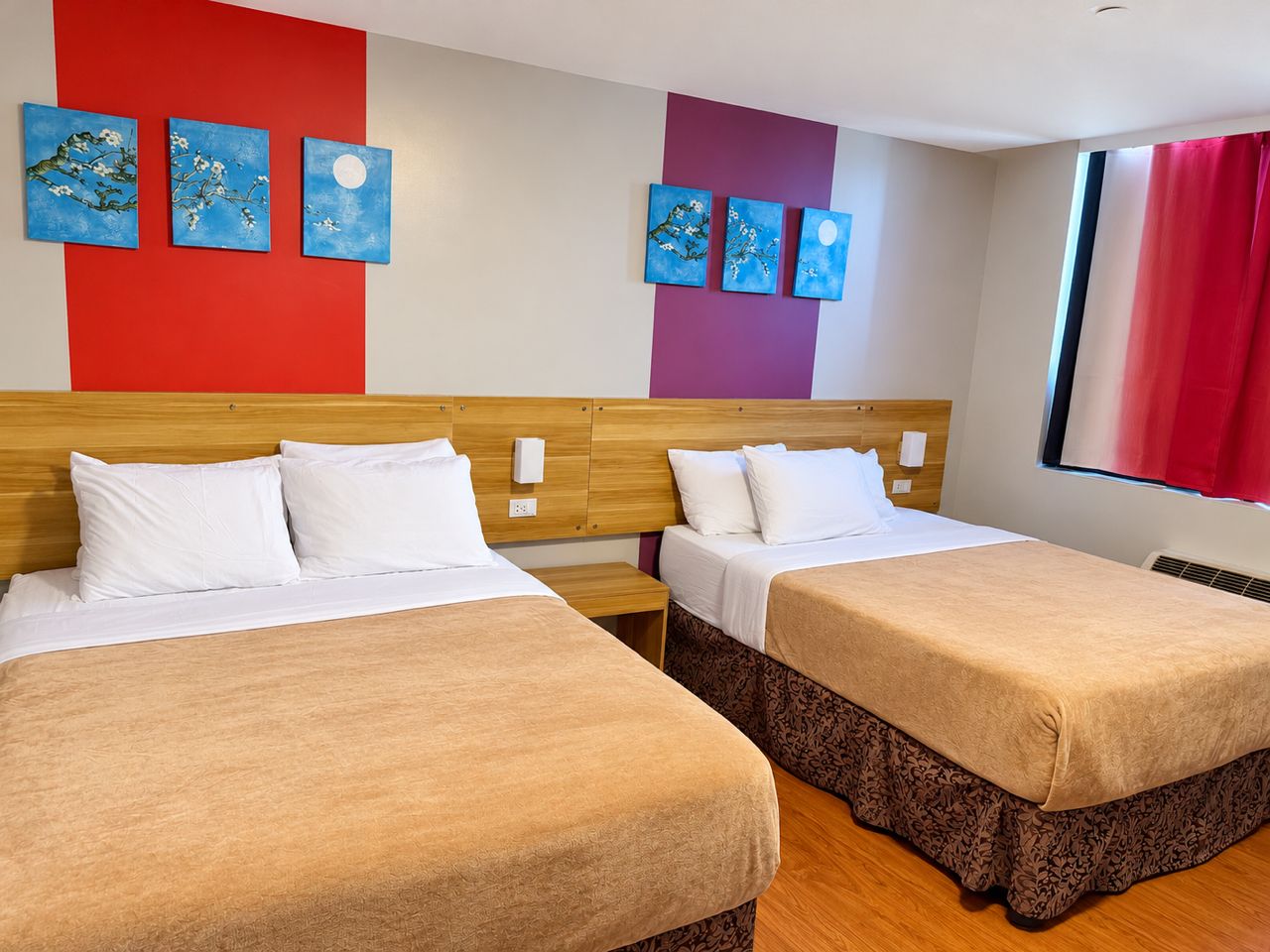 A hotel room with two beds, a red and purple wall, and artwork.