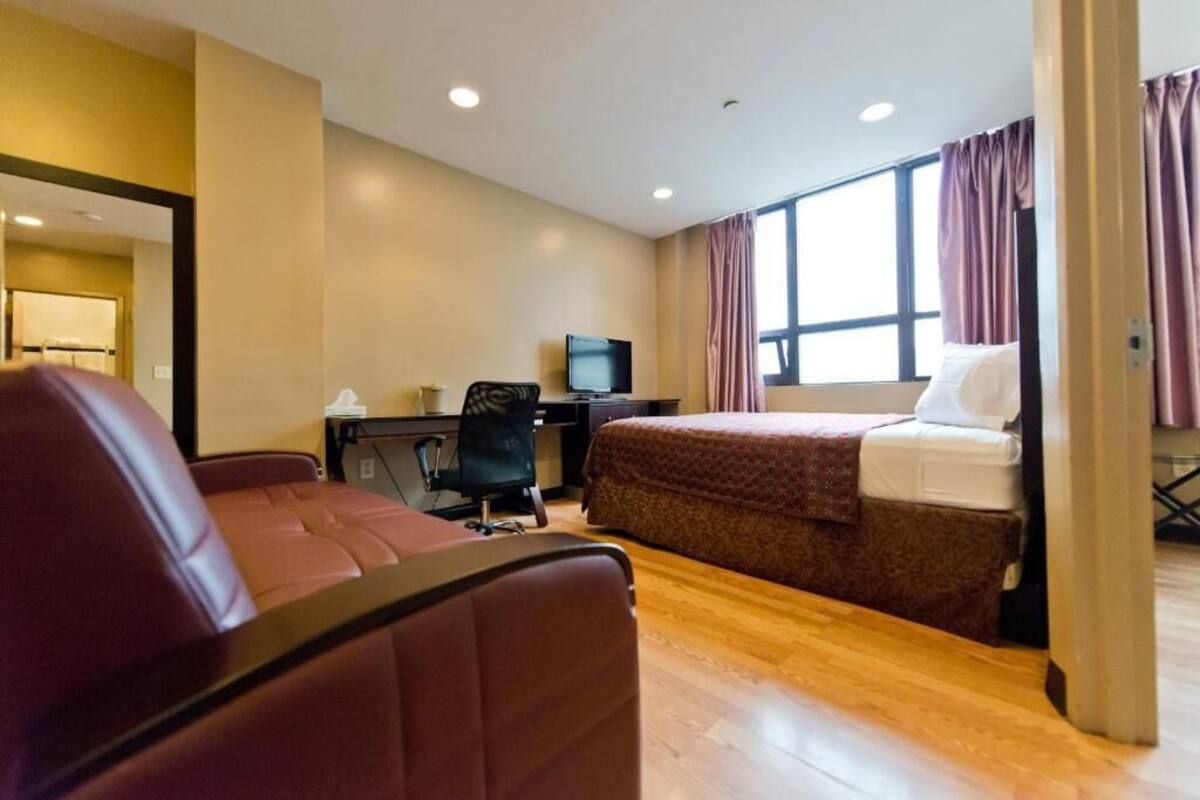 A hotel room with a bed, a desk with a computer, a chair, and a television.