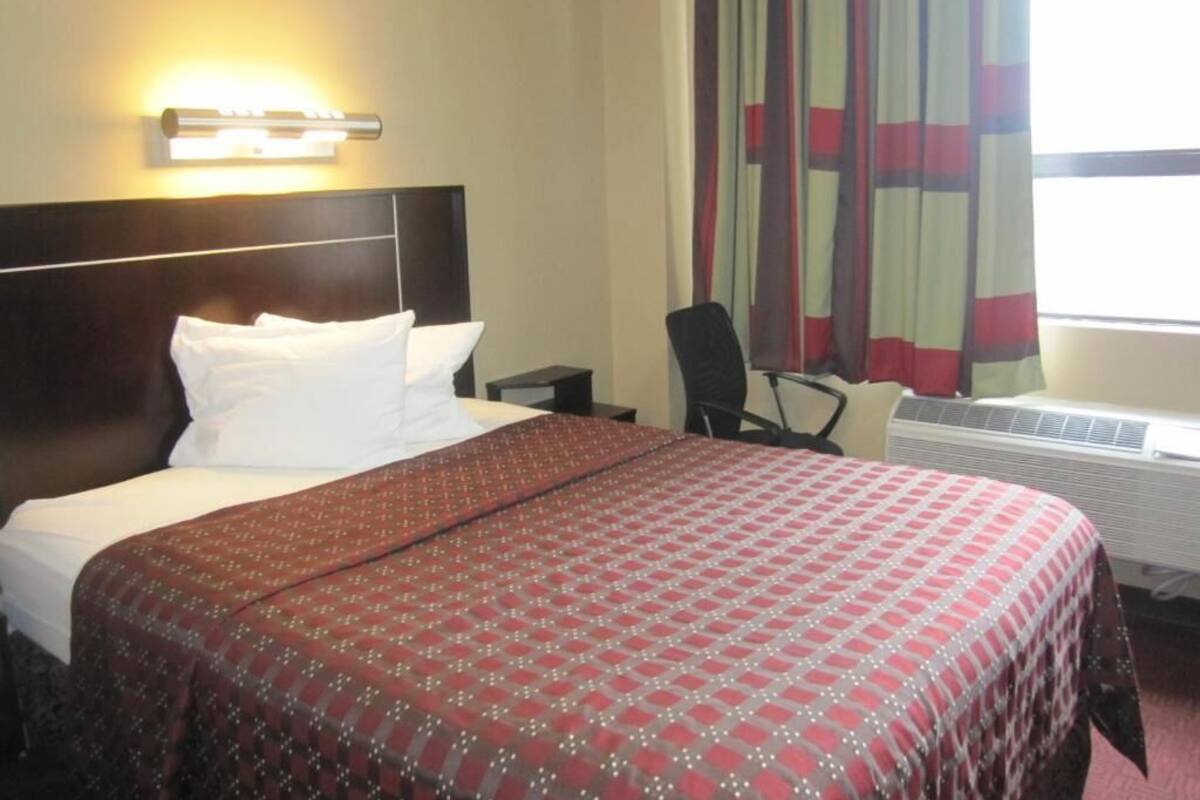 A hotel room with a large bed, a nightstand, a chair, and a window with curtains.