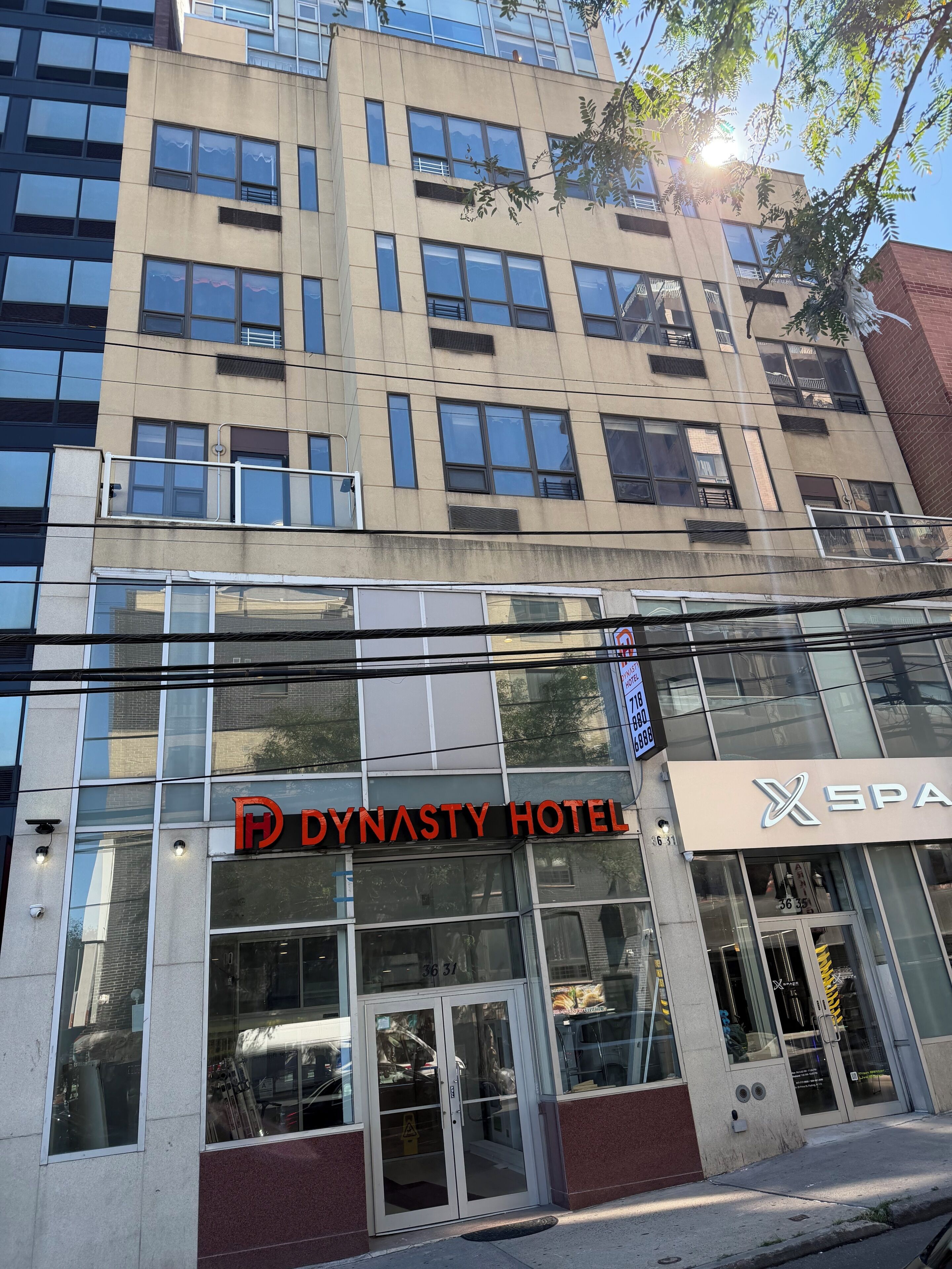 Un hotel con fachada moderna, grandes ventanales y un letrero llamativo que dice 'DYNASTY HOTEL'.
