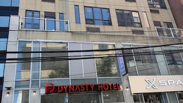 Un hotel con fachada moderna, grandes ventanales y un letrero llamativo que dice 'DYNASTY HOTEL'.