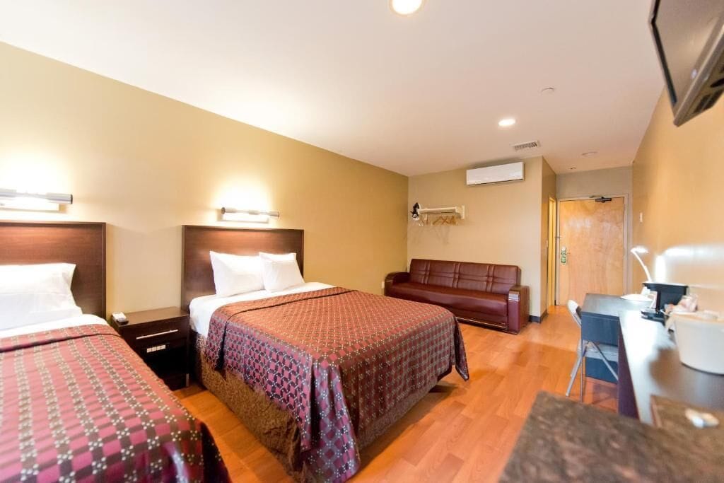 A hotel room with two beds, a sofa, a desk, and a TV.