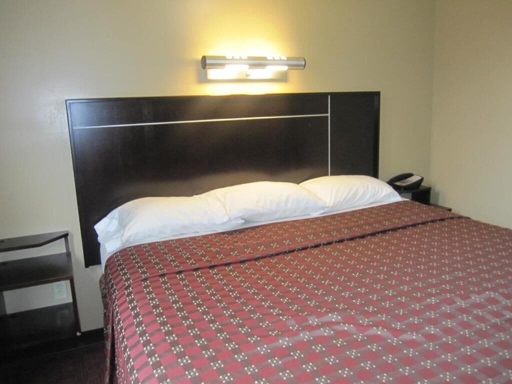 A hotel room with a bed, a nightstand, a lamp, and a wall-mounted light fixture.
