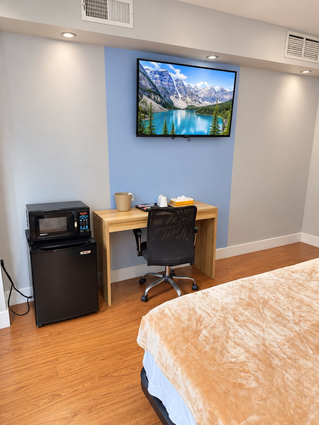 Une chambre d’hôtel équipée d’un lit, d’un bureau avec un ordinateur, d’un four à micro-ondes et d’un téléviseur diffusant un paysage de montagne.