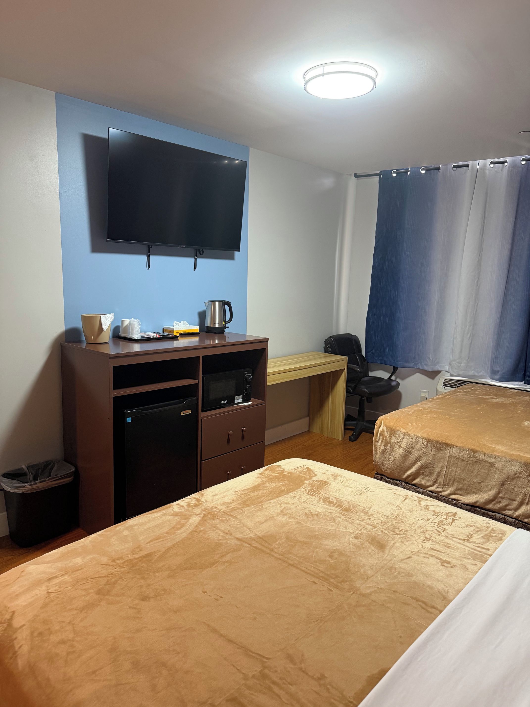 A hotel room with a bed, a desk with a computer, a television, and a window with curtains.