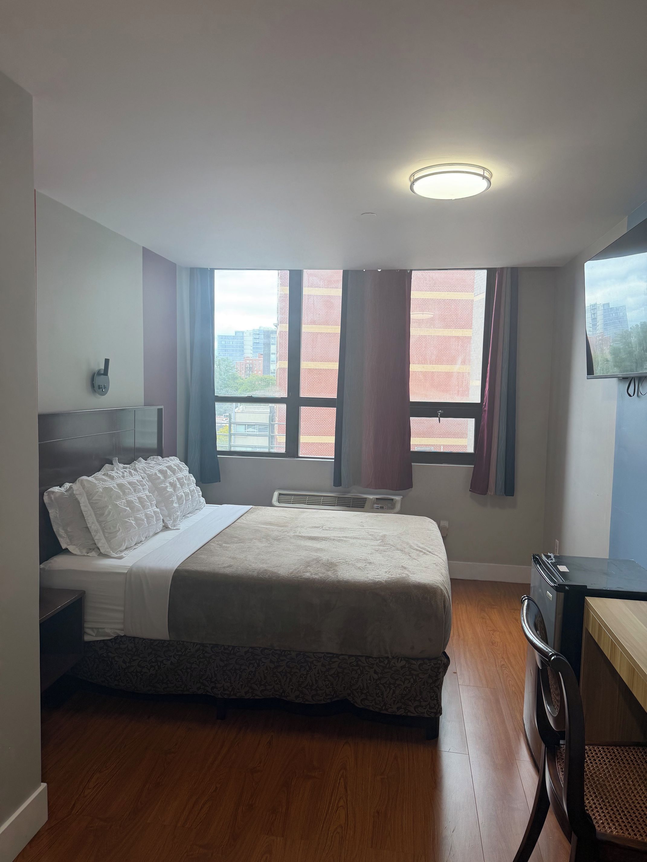 Habitación de hotel con cama, escritorio, ventana con cortinas y equipo de aire acondicionado.