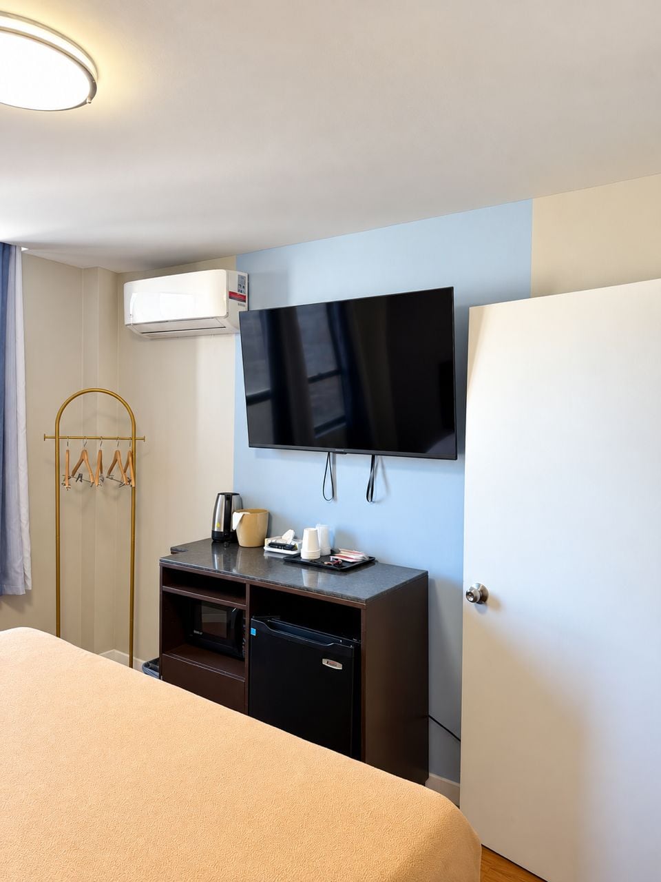 A hotel room with a bed, a desk with a flat-screen TV, a minibar, and a wardrobe.