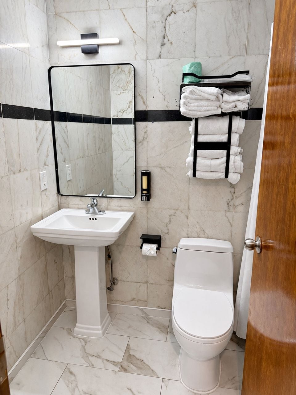 A bathroom with a white sink, a toilet, a mirror, and a towel rack with folded towels.
