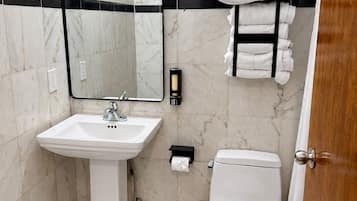 A bathroom with a white sink, a toilet, a mirror, and a towel rack with folded towels.