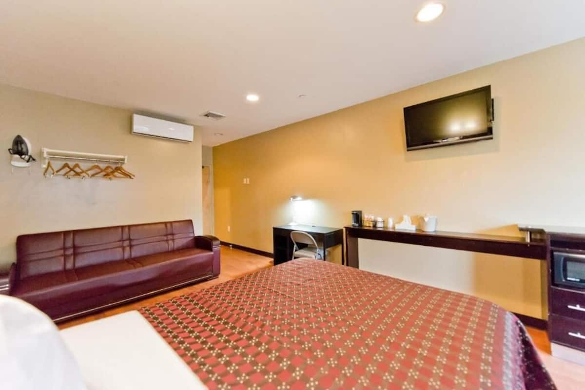 A hotel room with a bed, a desk, a TV, a sofa, and a coat rack.