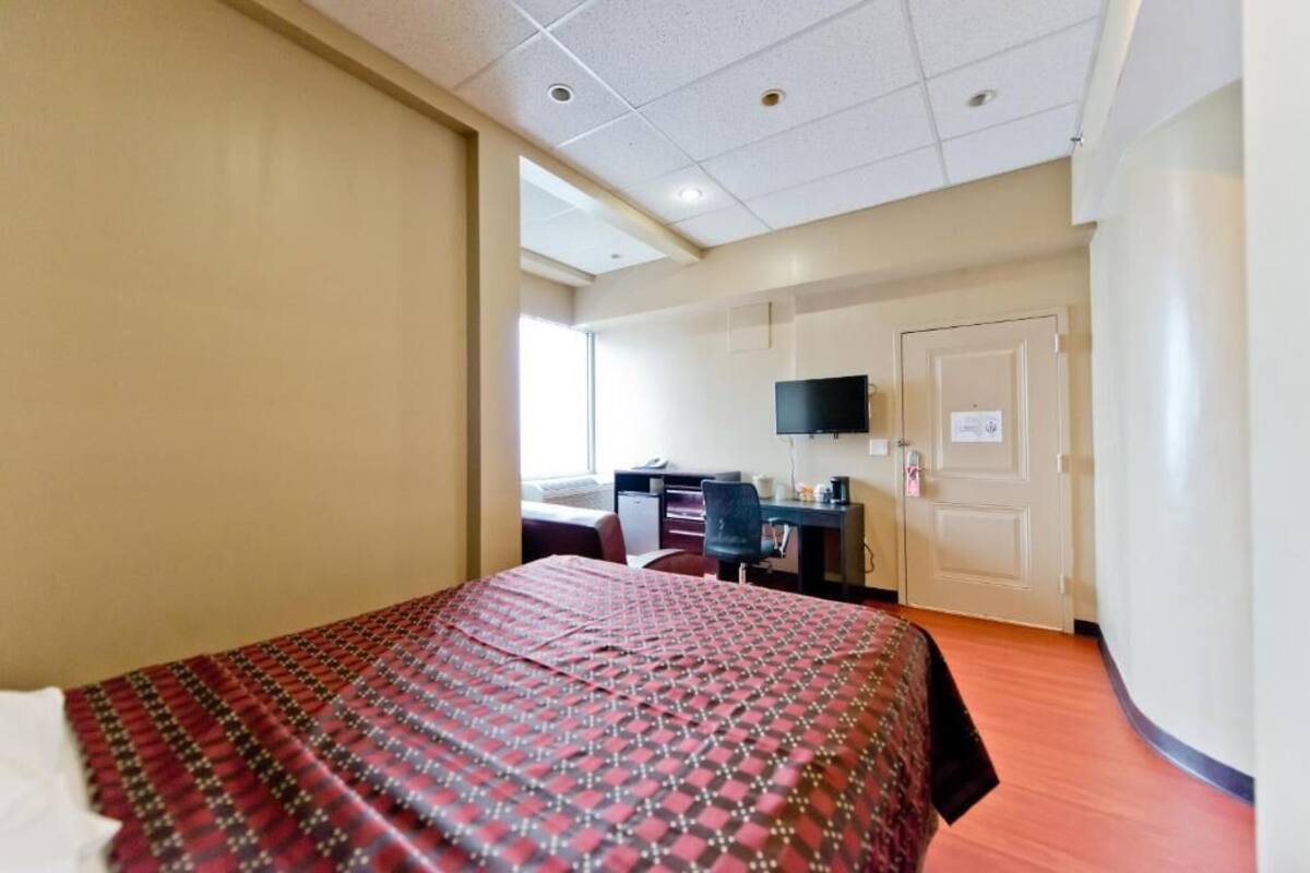 A hotel room with a bed, a desk, a chair, a television, and a door.