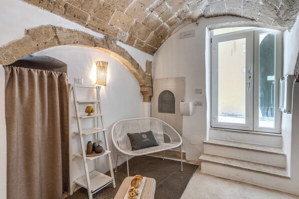 Ein Zimmer mit Ziegeldecke, einem weißen Stuhl mit Kissen, einem Regal mit Dekorationsobjekten und einem Fenster mit Blick.