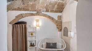 A cozy room with a white wicker chair, a shelf with decorative items, a brick archway, and a curtain. - La Cummare - Le Case di Valentina (Gallipoli)